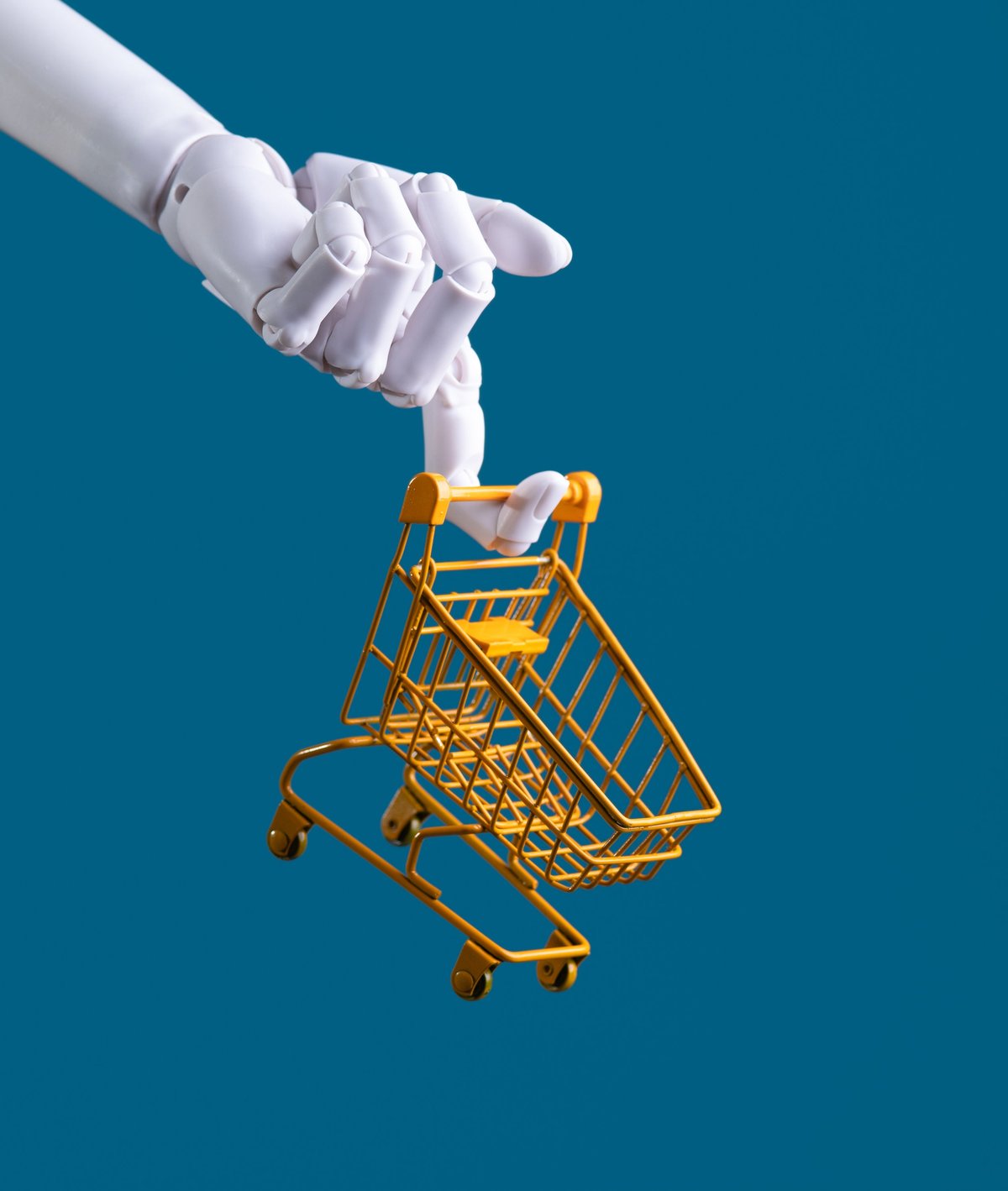 Robot hand holding a miniature shopping cart, representing automated ecommerce and retail technology
