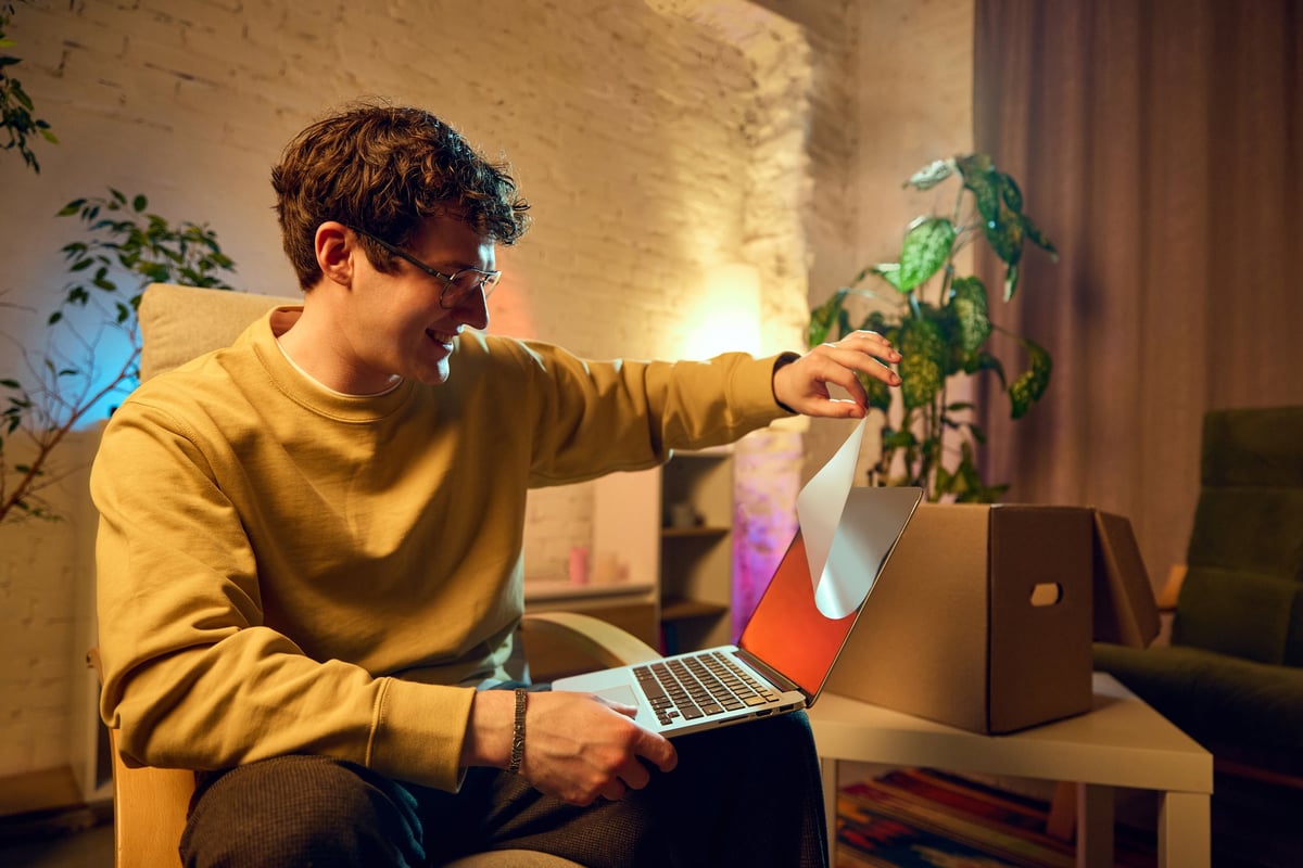 Man peeling a protective layer from a new laptop screen, illustrating unboxing a new device purchased online
